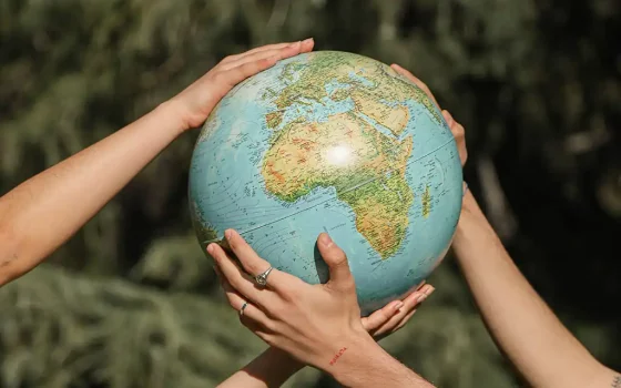two pairs of hands holding up a globe with greenery in the background