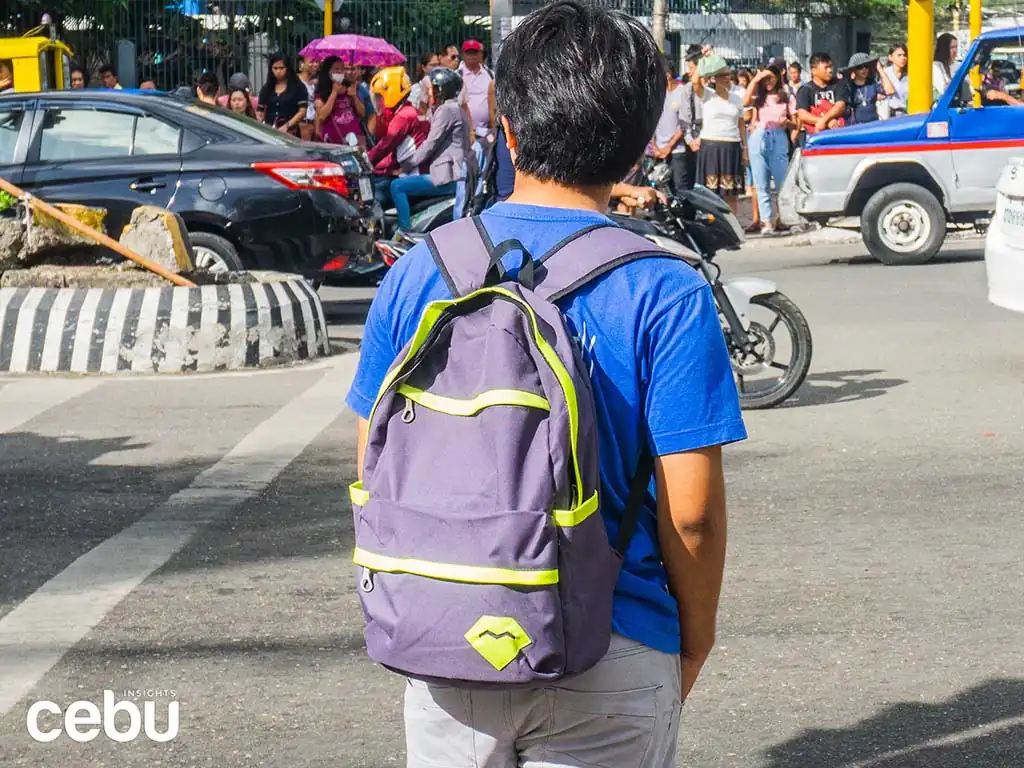 Man carrying a backpack of travel essentials waiting to cross the street in Cebu City